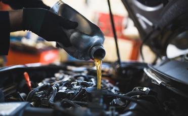 close up hands of mechanic pouring engine oil into a car